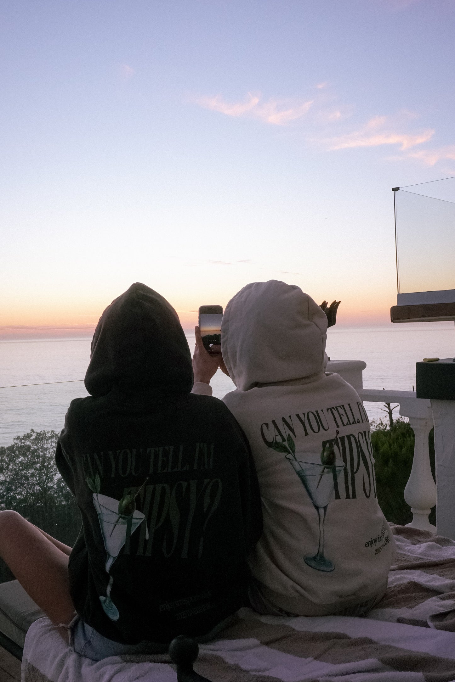 Two people sitting on a rooftop at sunset, one holding a phone.