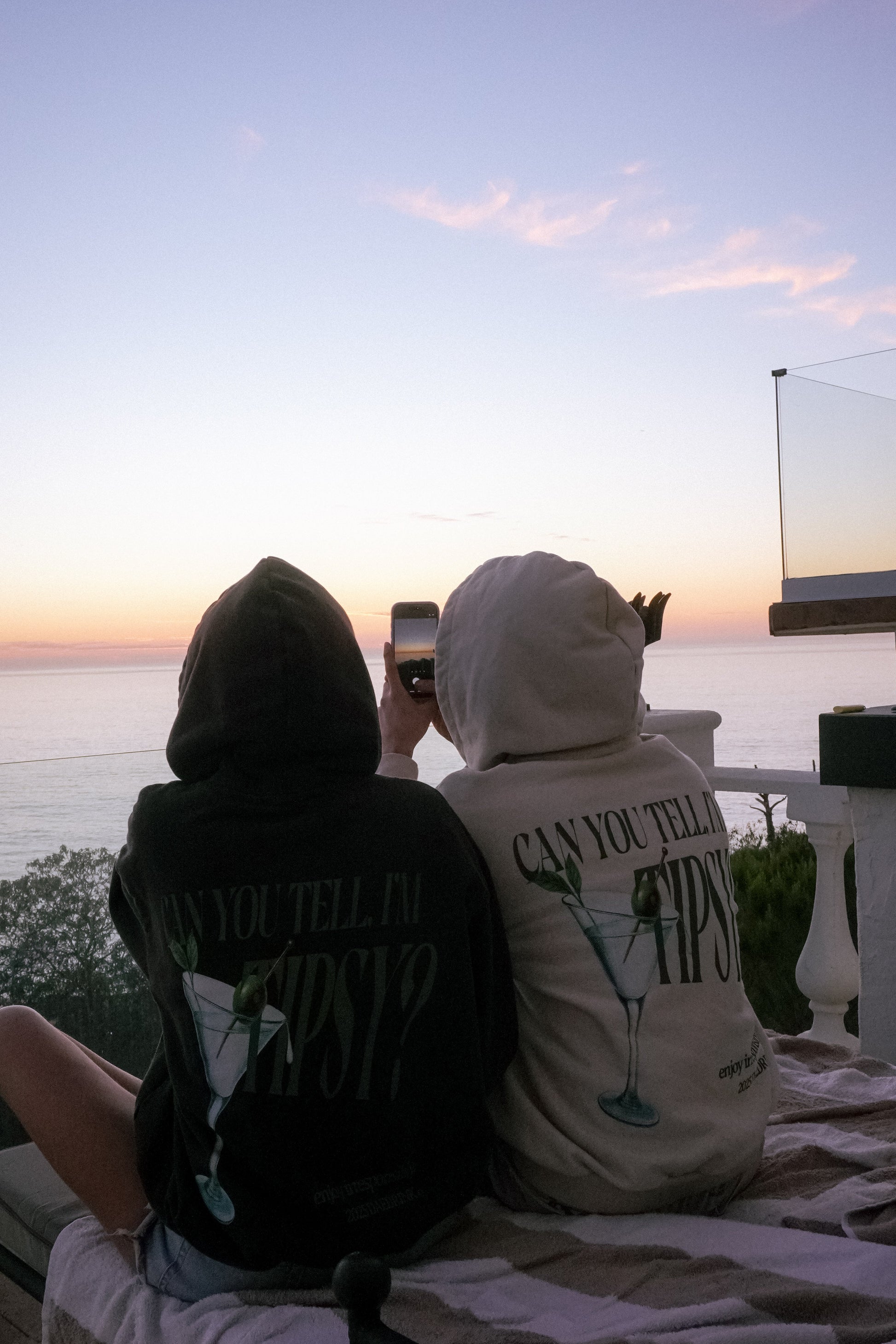 Two people sitting on a rooftop at sunset, one holding a phone.